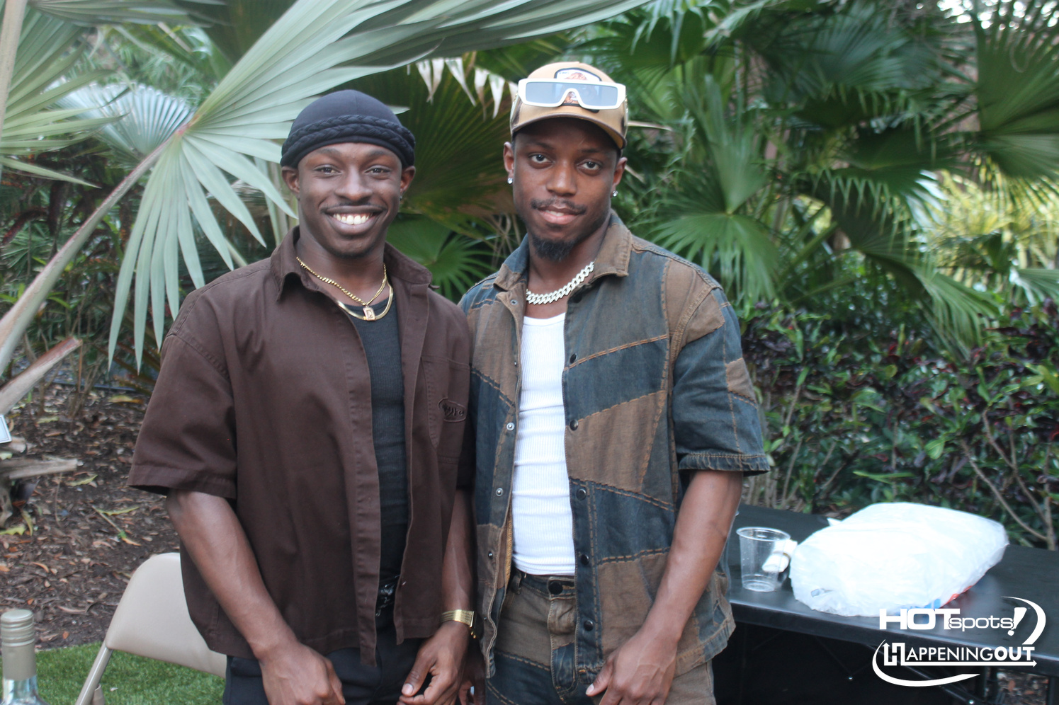 Two men posing outdoors among lush tropical plants, smiling at the camera.
