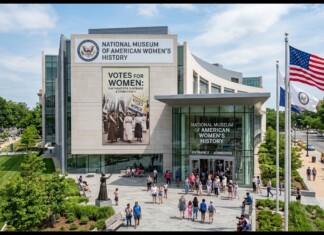 Front view of the National Museum of American Women’s History with large banner and American flag outside; people gather at the entrance on a sunny day.