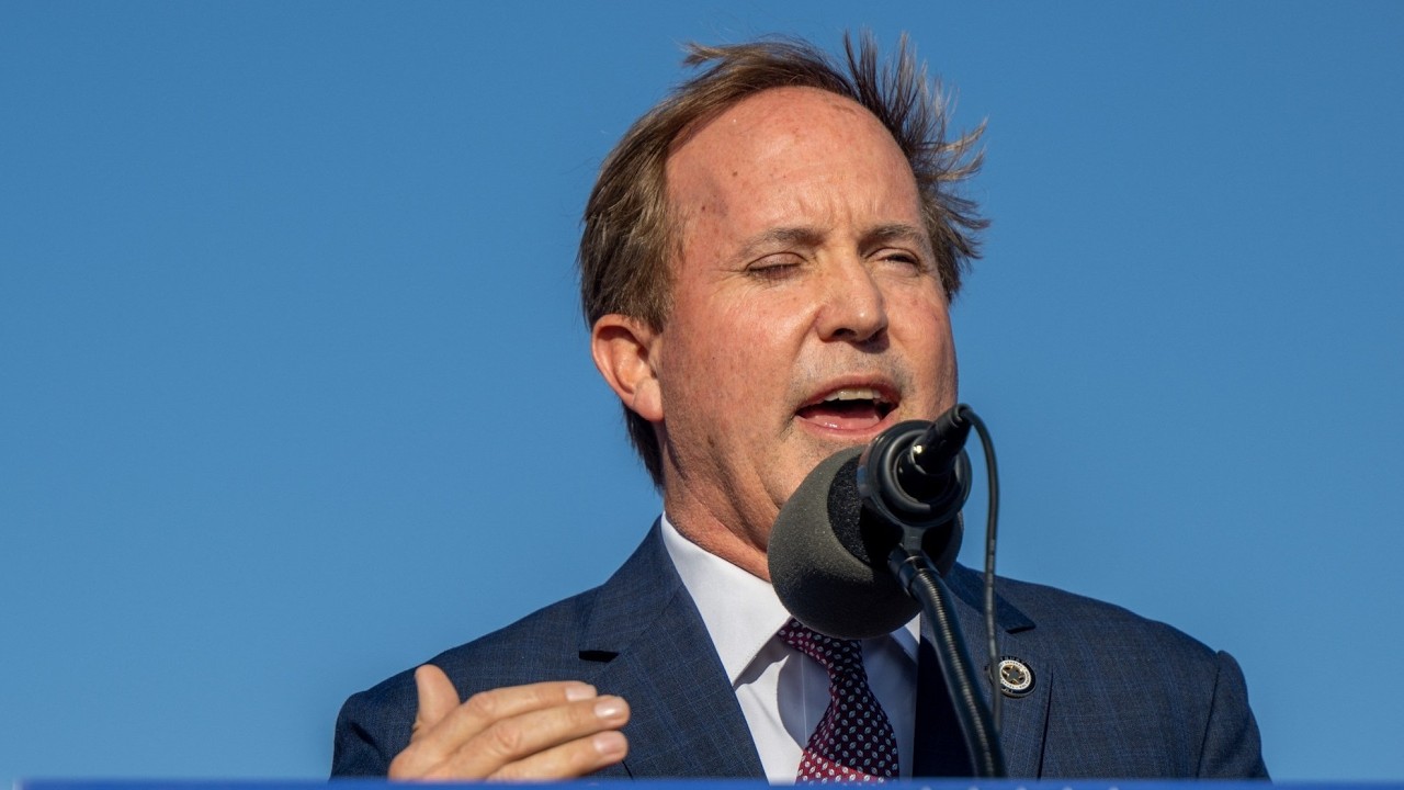 Man in a blue suit delivering a speech at a microphone outdoors against a clear blue sky?