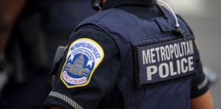 Metropolitan Police officer in navy uniform, back patch reads METROPOLITAN POLICE, close-up view.