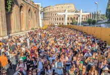 Rome Pride Faces Backlash Over Ban on Jewish LGBTQ Groups Huge crowd of people gathered outdoors at a festival or concert near the Colosseum in Rome, with yellow barriers along the right side and clear blue sky above.