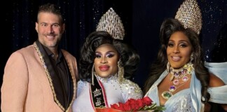Three drag performers pose on stage; center winner in a silver gown and crown holds a red rose bouquet, flanked by two smiling contestants.