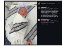 Newborn baby swaddled in a striped hospital blanket with a pink bow headband, lying in a hospital bed. That the image shows a birth announcement in a social post context.