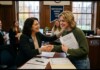 Two women shake hands across a desk during a signing ceremony in a campus office, with colleagues watching in the background and a banner reading 'Empowering Women Since 1837'.