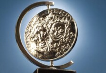 Shiny silver coin mounted in a curved metal stand against a blue sky background, seen from the side.