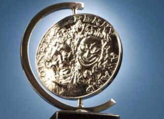 Shiny silver coin mounted in a curved metal stand against a blue sky background, seen from the side.