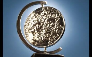 Shiny silver coin mounted in a curved metal stand against a blue sky background, seen from the side.