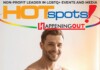 Smiling man in front of a colorful banner that reads HOTspots and Happening Out, promoting LGBTQ+ events and media.