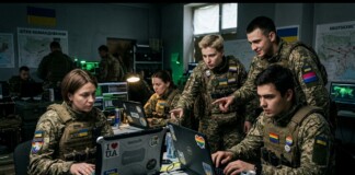 Group of Ukrainian soldiers in a dim control room collaborating on laptops with patches and stickers visible on gear.