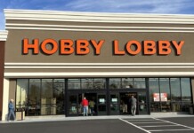 Hobby Lobby storefront with large orange letters and glass doors, customers entering the store on a sunny day.