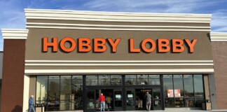 Hobby Lobby storefront with large orange letters and glass doors, customers entering the store on a sunny day.