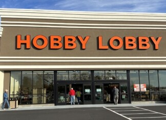 Hobby Lobby storefront with large orange letters and glass doors, customers entering the store on a sunny day.