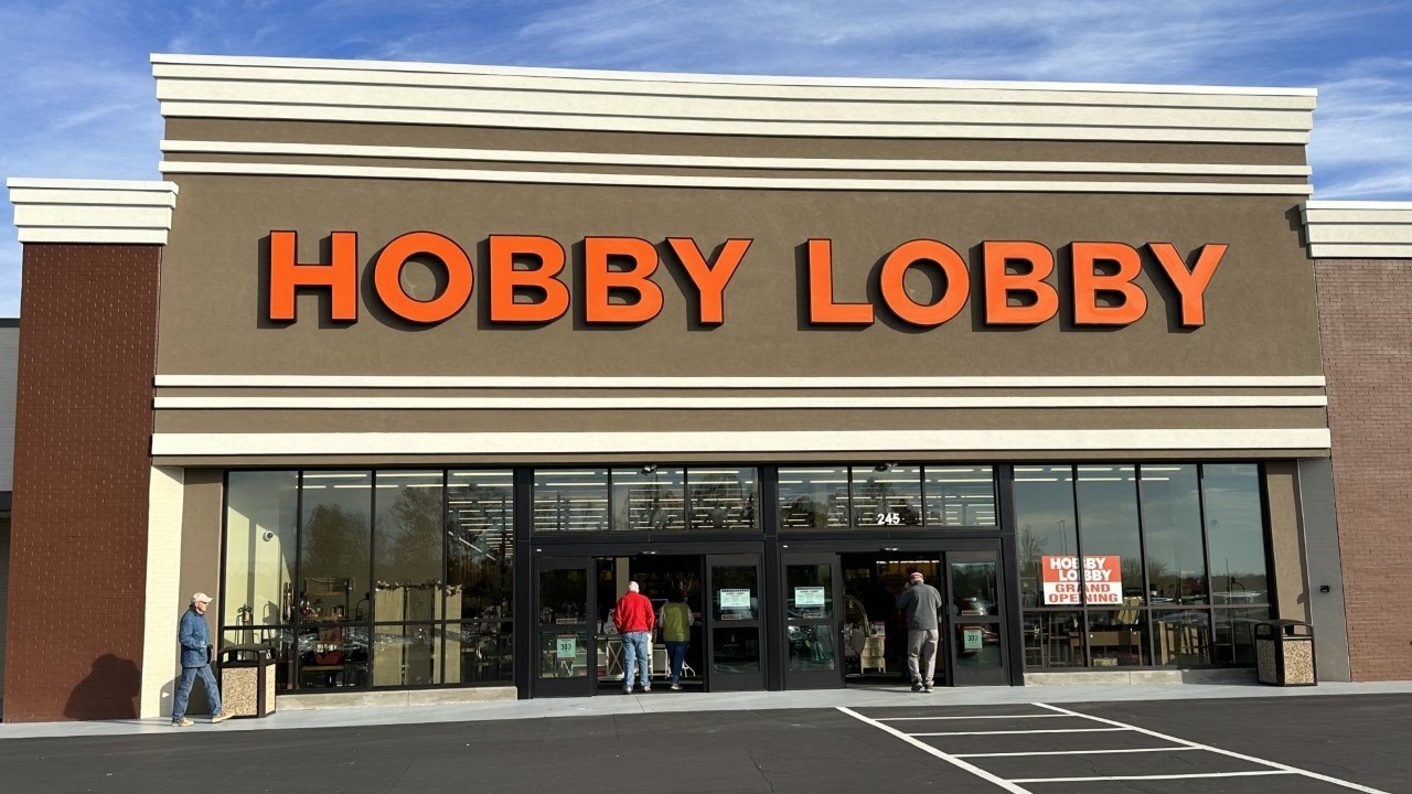 Hobby Lobby storefront with large orange letters and glass doors, customers entering the store on a sunny day.
