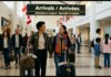 Two travelers walk hand in hand with rolling suitcases through a busy airport arrivals hall, smiling as they go.