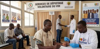 HIV testing center scene: a nurse in gloves prepares a rapid test for a man sitting at a table, with a large HIV testing banner behind them and people waiting nearby.