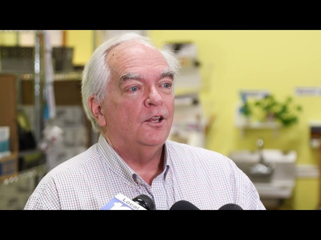 Poverello CEO Thomas Pietrogallo Dies After Decades of HIV and Community Advocacy Older man with white hair speaks to reporters in a yellow-walled room, microphones in front of him.