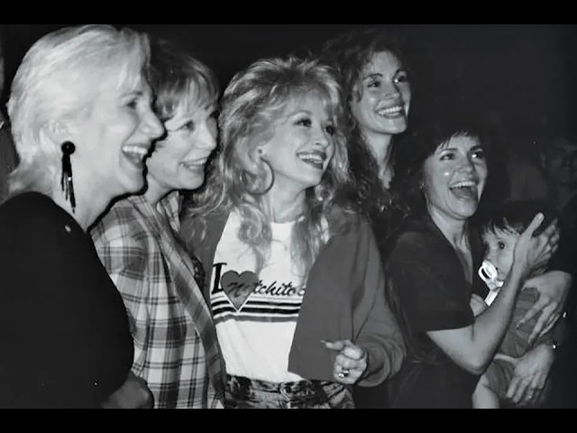 Five women posing and laughing together at a social event, enjoying the moment in a candid black-and-white photo.