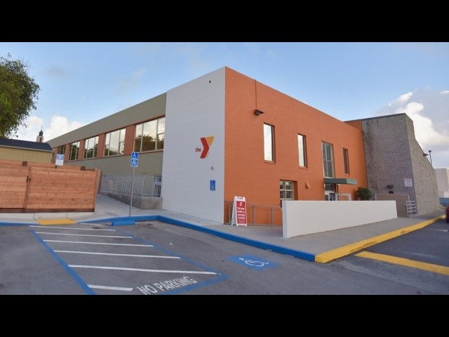 Exterior of a YMCA building with orange and white walls, blue curb, and disabled parking spaces in the foreground.