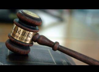 Wooden judge's gavel with a brass band reading 'People's Court' resting on a desk in a courtroom setting.