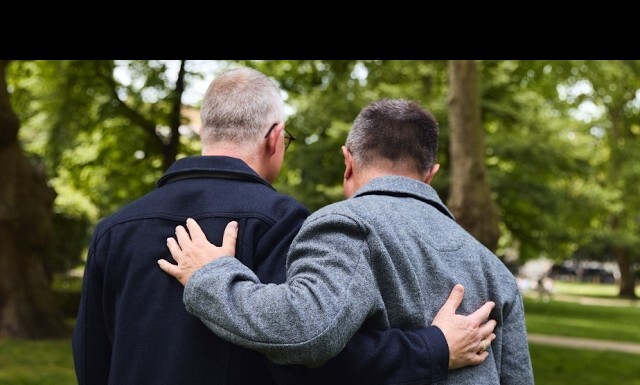 A Broward County Perspective for Older Americans Awareness Month Two men walk with arms around each other in a green park, conveying friendship and support.