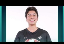 Smiling young person in a dark jersey holding a soccer ball against a white studio background.