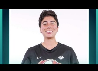 Smiling young person in a dark jersey holding a soccer ball against a white studio background.