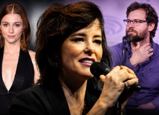 Female singer in front holding a microphone, flanked by a red-haired woman in black on the left and a bearded man with glasses on the right at a panel event.
