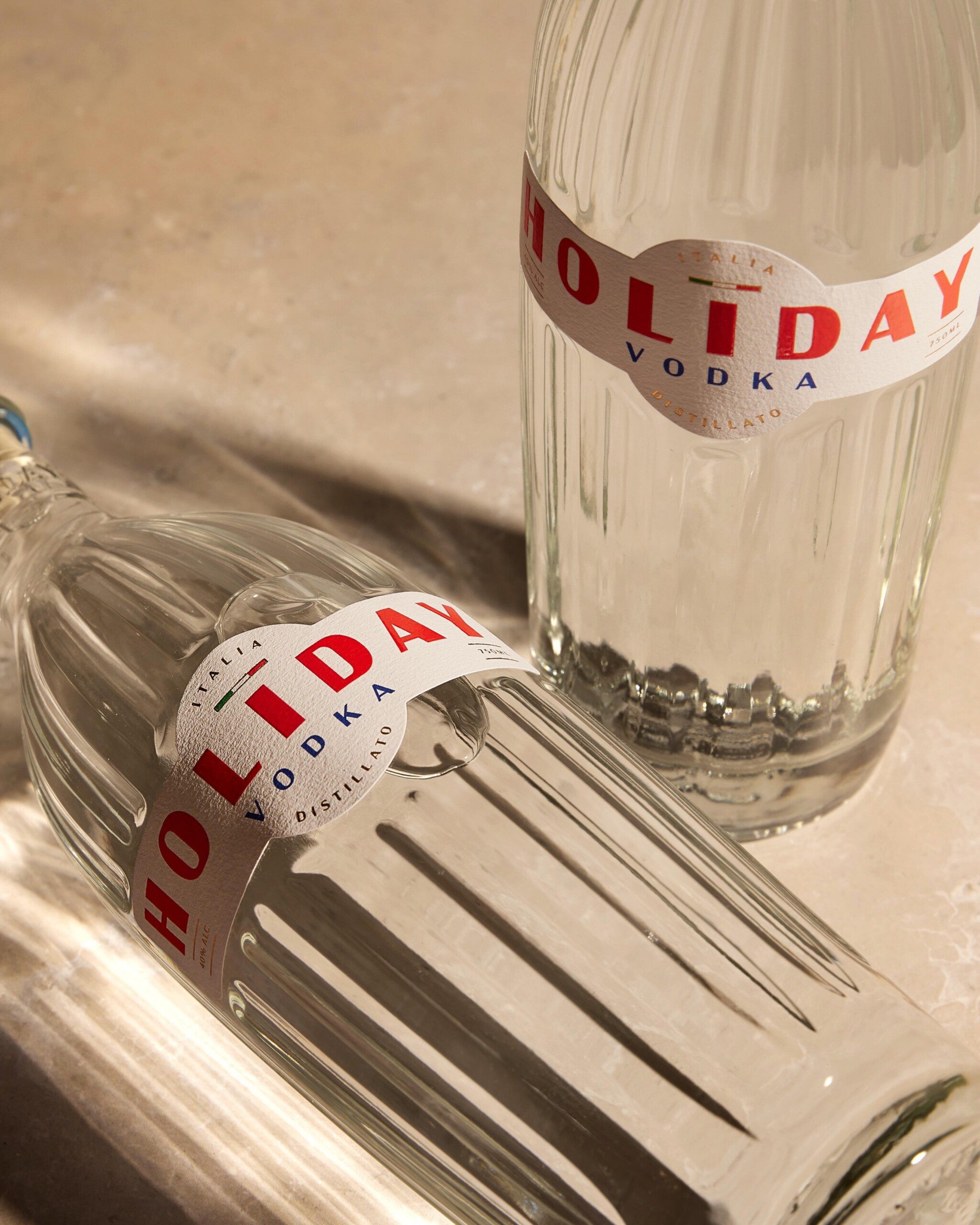 Close-up of a clear vodka bottle with a curved white label reading HOLIDAY VODKA in red letters and Italian flag accents on a countertop.