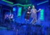 Two actors in vintage costumes headline a blue-lit stage, posing with open arms amid fog.