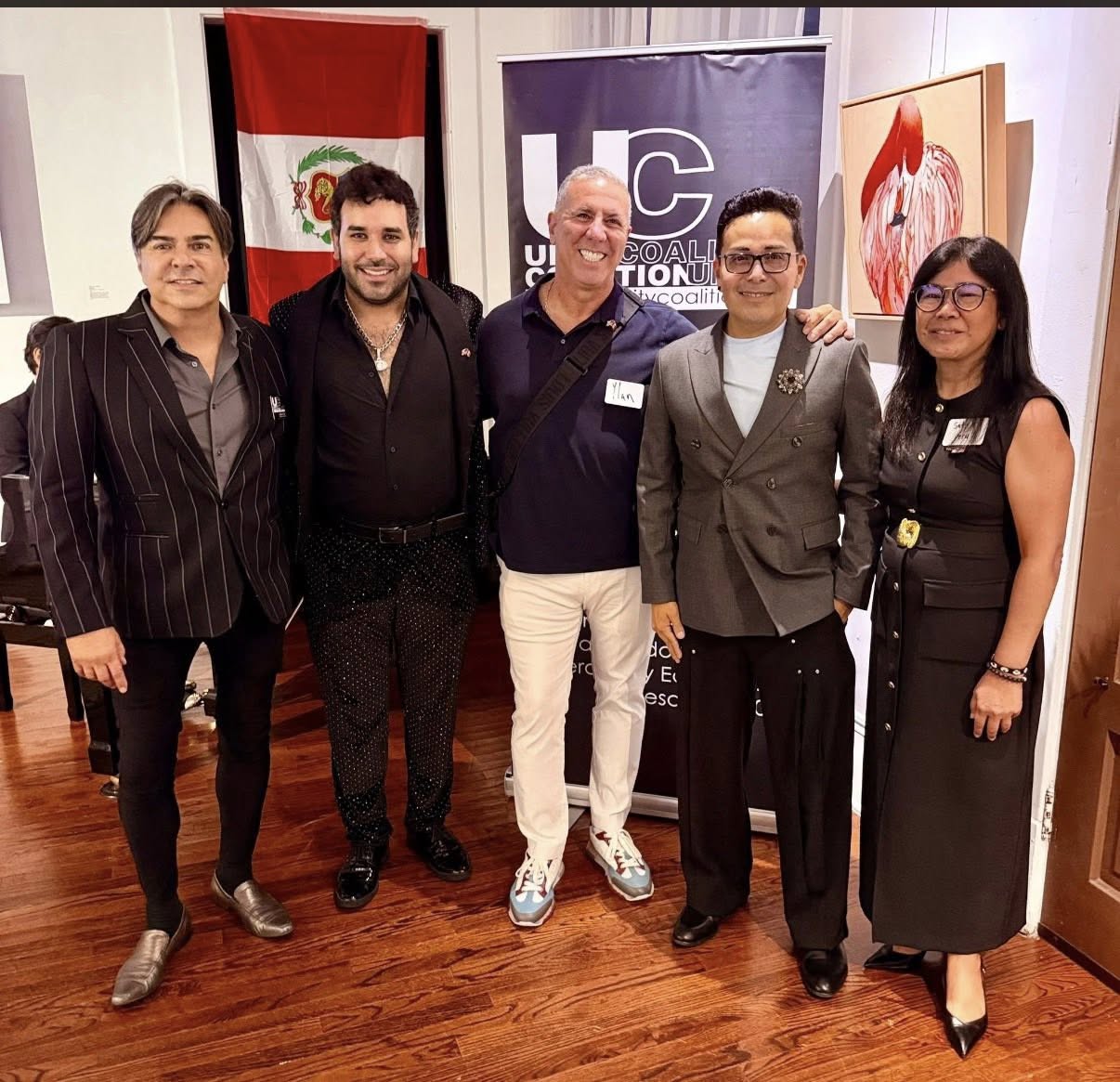 Five people in formal/smart-casual outfits pose together at an event in a gallery, with a Peruvian flag and a UC banner in the background.