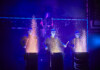 Blue Man Group – Comes to the Broward Center, June 11-14 Four performers in blue-lit suits drum on stage, sparks flying from each drum as part of a dramatic percussion act.