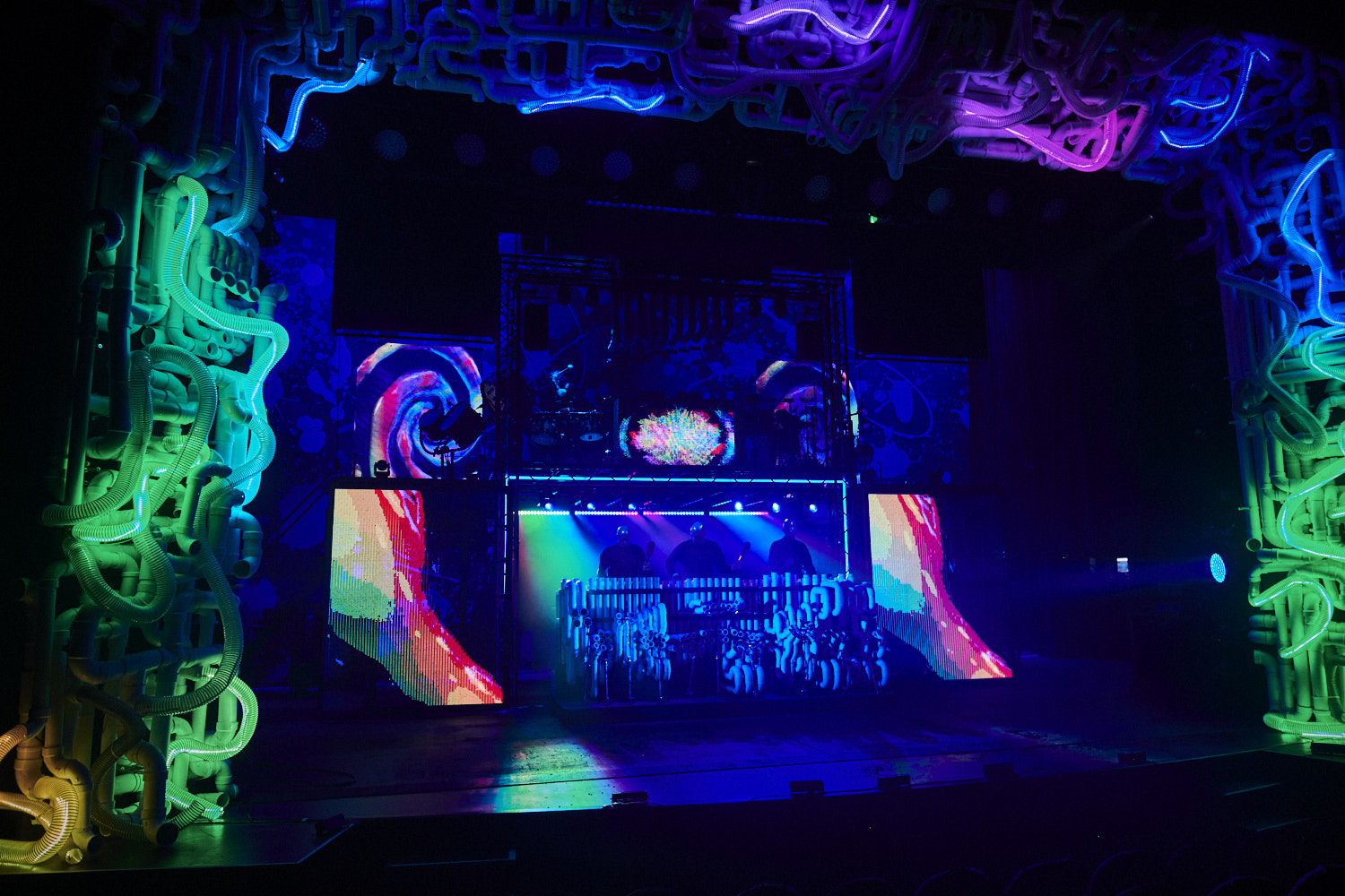 Stage at a neon-lit club with a DJ booth, colorful LED panels, and tangled tubular lighting surrounding the performance area.