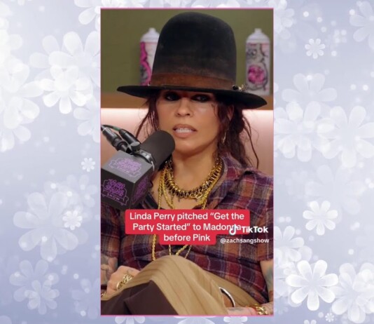 Woman wearing a wide black hat and plaid shirt speaks into a microphone during a radio interview, with a red caption about Linda Perry visible on screen.