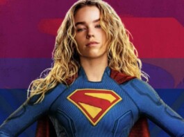 Woman in a blue Superman costume with red cape, hands on hips, against a rainbow-striped background.