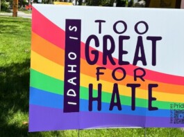 Rainbow Pride sign outdoors reading 'Too Great for Hate' with 'Idaho' vertical; Pride resources QR code in the lower corner.