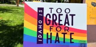 Rainbow Pride sign outdoors reading 'Too Great for Hate' with 'Idaho' vertical; Pride resources QR code in the lower corner.