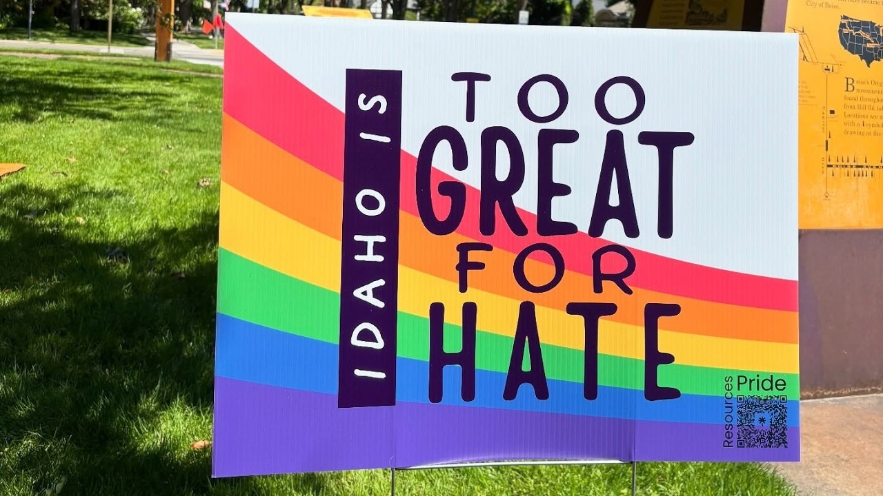 Rainbow Pride sign outdoors reading 'Too Great for Hate' with 'Idaho' vertical; Pride resources QR code in the lower corner.