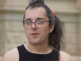 Trans Woman Named Rihanna Kelver Charged Despite Wyoming ‘Stand Your Ground’ Self-Defense Law Person with purple glasses and a septum piercing looks to the side, wearing a black sleeveless top outdoors near a stone building.