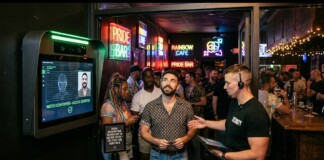 Crowded neon-lit bar scene with Pride signs; a man in a patterned shirt listens to a staffer holding a tablet near a facial-recognition kiosk on the left.