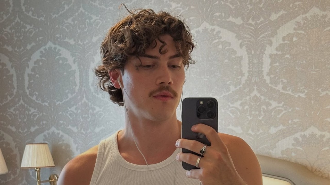 Jack Innanen Forced to Pass on Heated Rivalry Season 2 Role Due to Scheduling Conflicts Young man in a white tank top taking a mirror selfie with earphones in a wallpapered bedroom