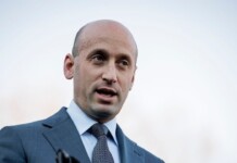 White House Official Faces Backlash Over Gender-Based Attacks on Texas Democrat James Talarico Bald man in a blue suit and patterned tie speaking outdoors, looking to the side.