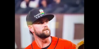 Baseball player wearing an orange jersey and black cap, looking off to the left on the field.