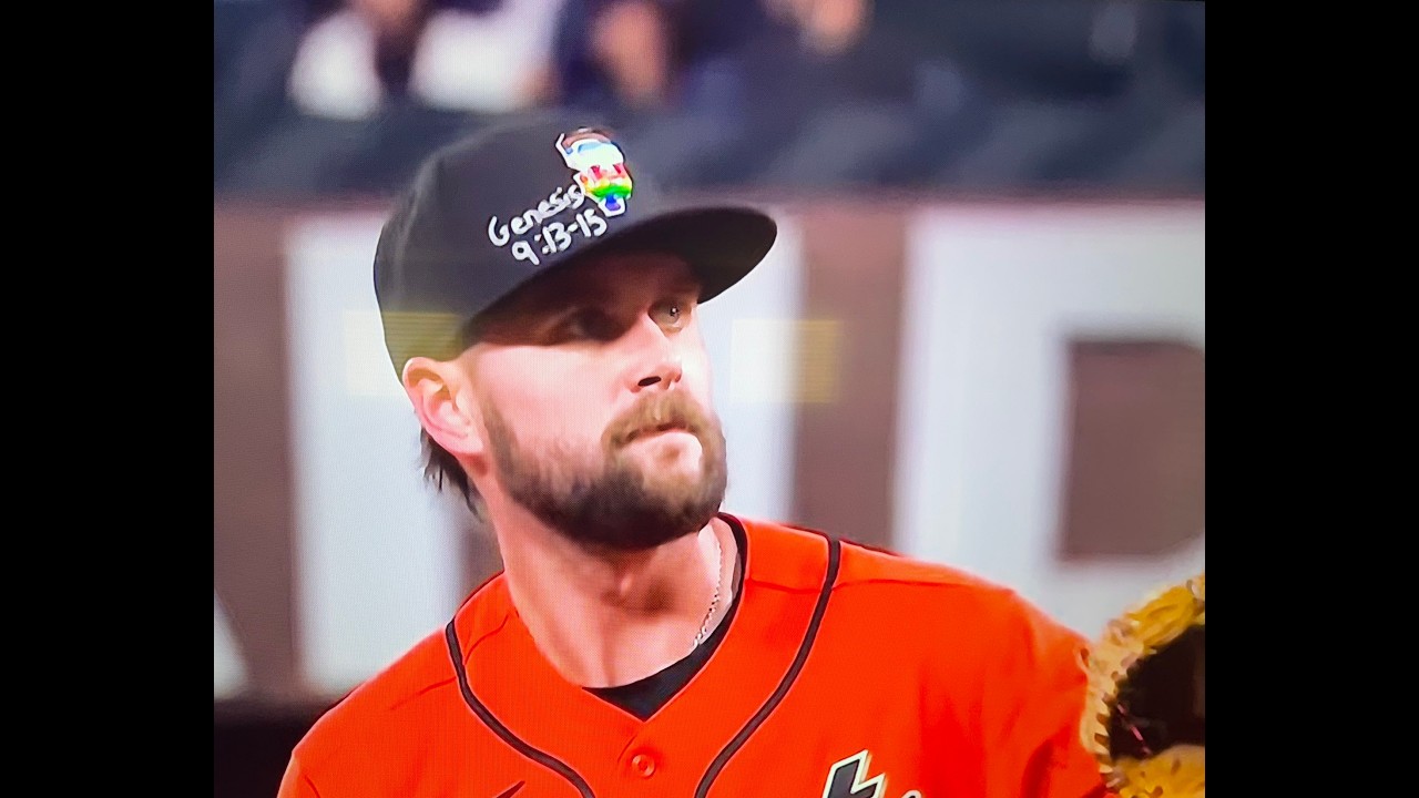 Baseball player wearing an orange jersey and black cap, looking off to the left on the field.