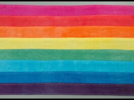 Rainbow horizontal flag with pink, red, orange, yellow, green, blue, and purple stripes laid flat, representing LGBTQ Pride.