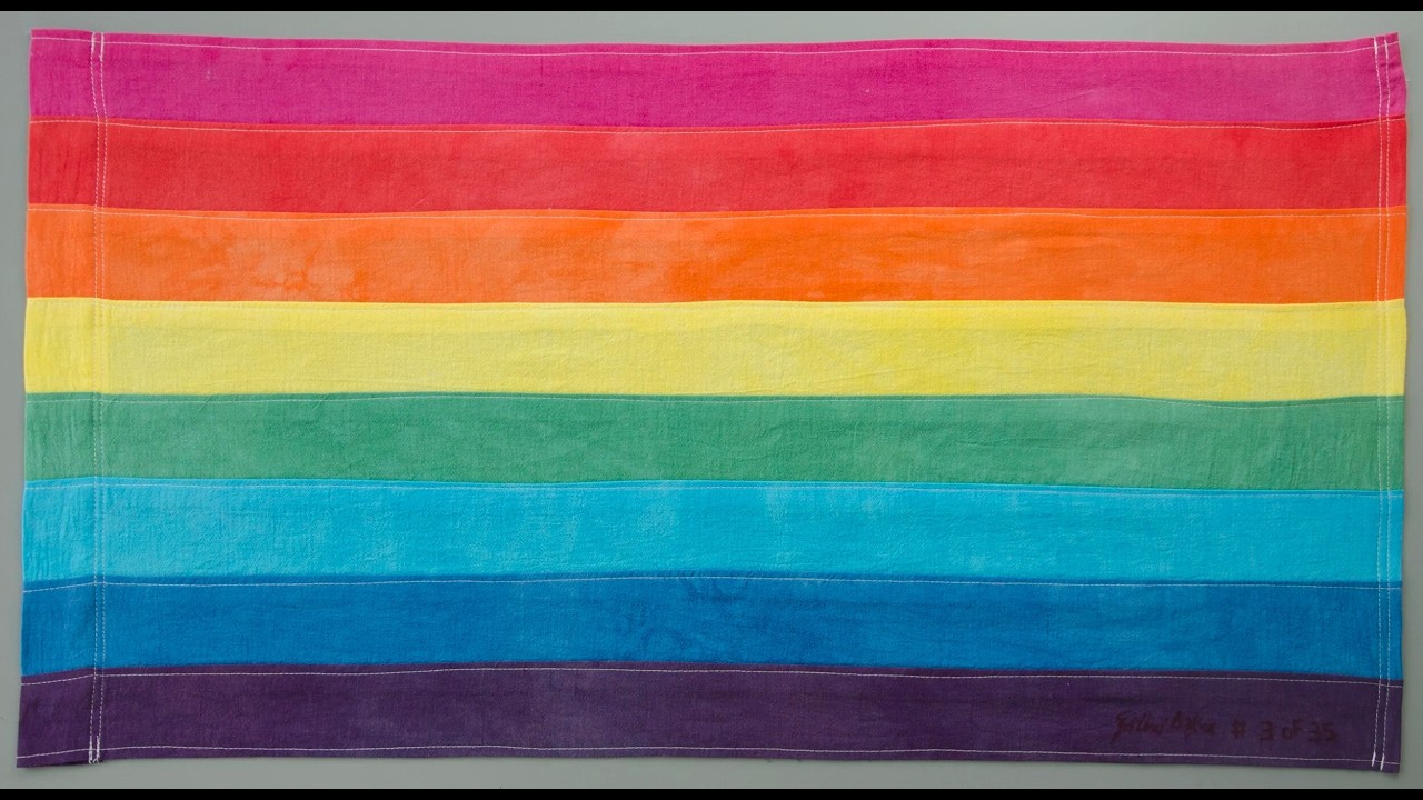 Rainbow horizontal flag with pink, red, orange, yellow, green, blue, and purple stripes laid flat, representing LGBTQ Pride.