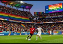 Soccer players contest the ball on a green pitch as a rainbow-filled crowd cheers in Pride Unity Stadium during the FIFA World Cup 1-1 Iran vs Egypt.