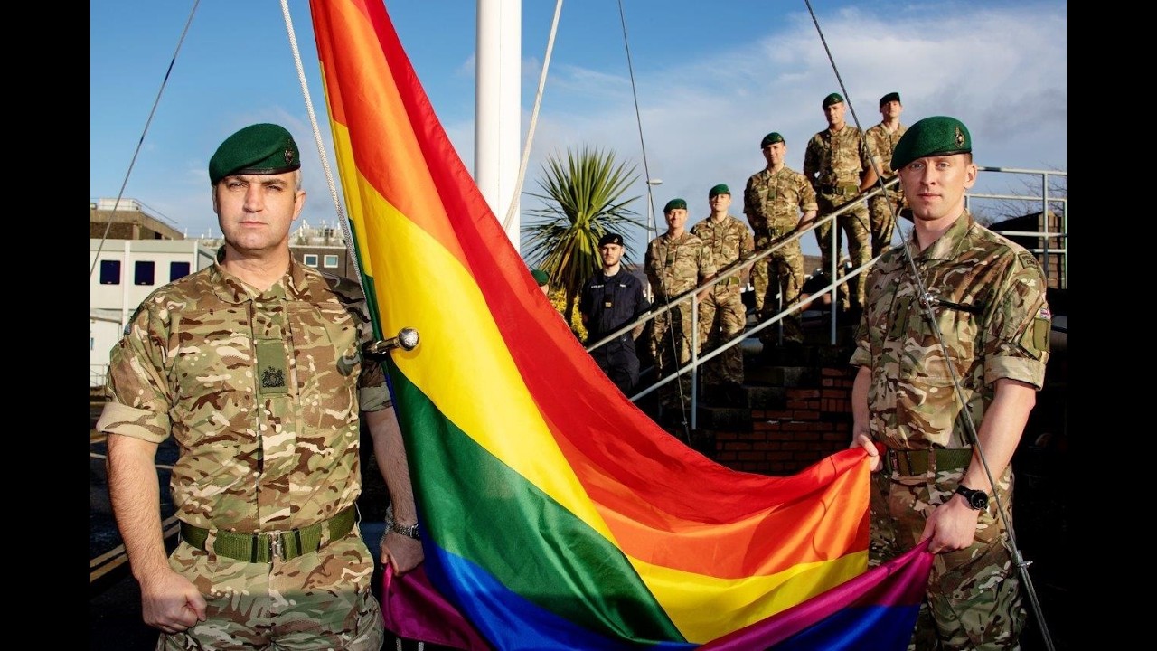 Time Running Out as 1,000 UK Veterans Could Miss Gay Ban Compensation Military personnel in camouflage hold a large rainbow Pride flag outdoors.