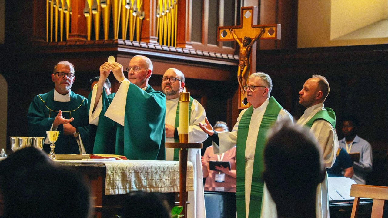 Messages of Hope and Healing as Cardinal Addresses LGBTQ+ Catholic Conference Priests in green liturgical vestments celebrate Mass at the altar; one priest elevates the Eucharist as others assist, with a crucifix and organ pipes in the background.