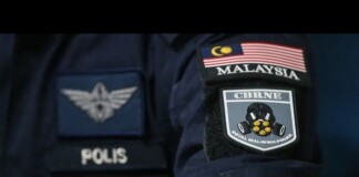 Close-up of police patches on a dark uniform, including a Malaysia flag patch and a POLIS badge on the sleeve.