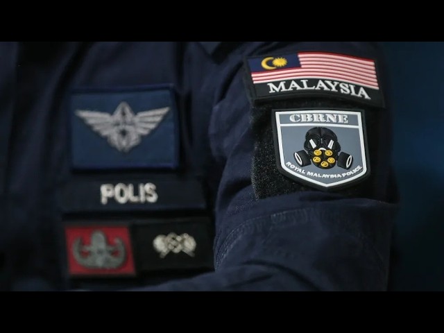 Close-up of police patches on a dark uniform, including a Malaysia flag patch and a POLIS badge on the sleeve.